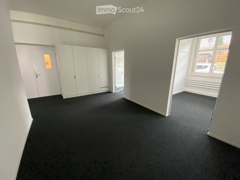 Empty room with white walls, black carpet, white cabinetry, and a glass partition. No furniture or equipment present.