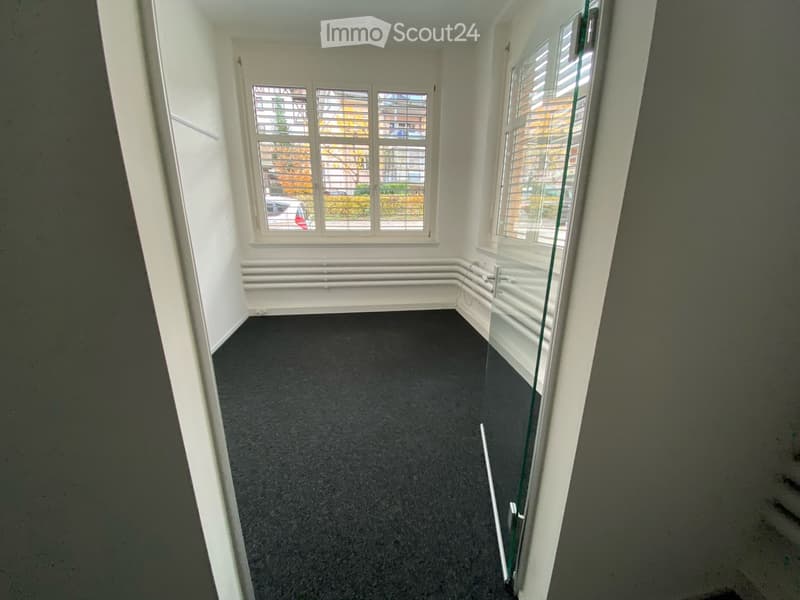 Empty room with grey carpet, white walls, large windows with blinds, and a glass door leading outside.