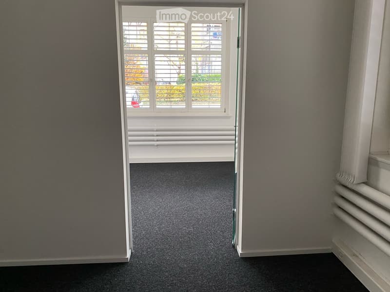 Empty room with grey carpeted floor, white walls, and a large window with blinds. No furniture or equipment present.