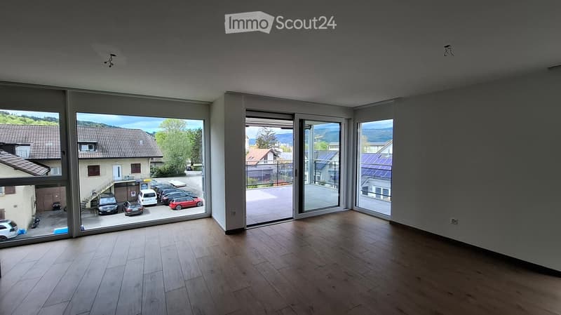 Empty room with wooden flooring, large windows, and sliding glass doors leading to a parking area.