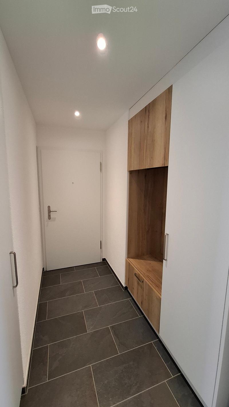 A narrow hallway with white walls, dark tiled floor, and built-in wooden storage unit on one side.