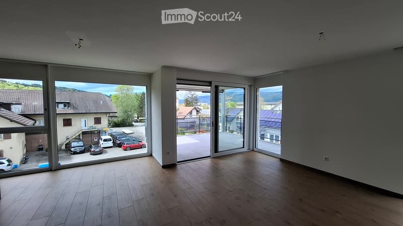 Bright, empty room with large glass sliding doors leading to a parking area, wooden flooring, and modern lighting fixtures.
