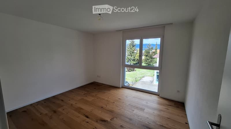 Empty room with wooden flooring, white walls, and large sliding glass door leading to a view of greenery and mountains.