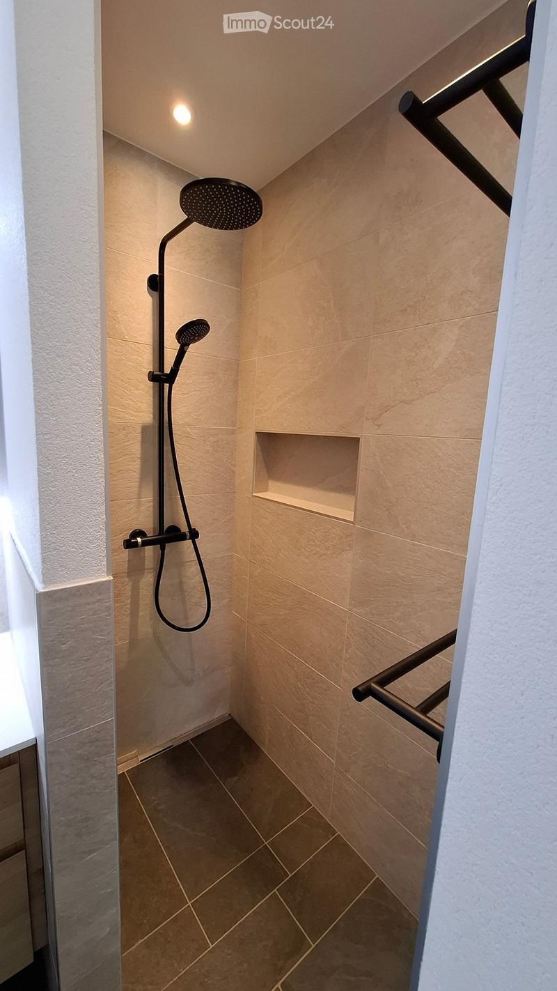 Modern shower area with beige tiles, a handheld showerhead, and a built-in shelf.