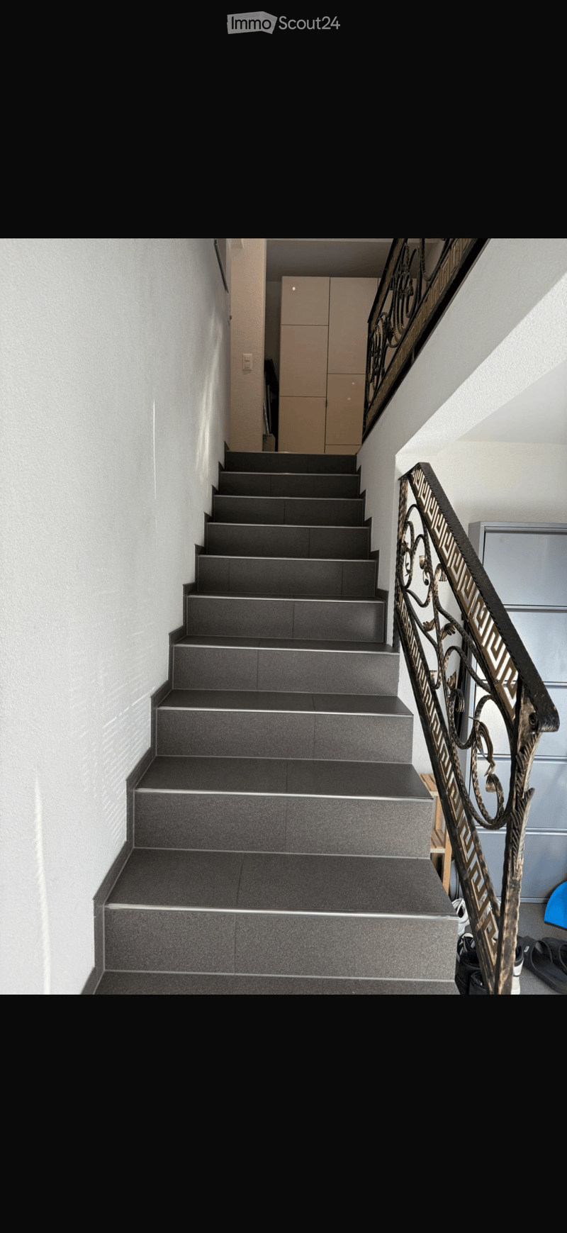 Modern staircase with dark grey tiles, metal railing, and white walls.