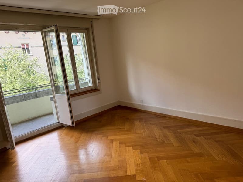 Empty room with wooden flooring, large windows, and a balcony view.
