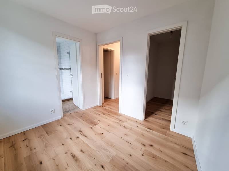 Empty room with light wooden flooring and white walls, featuring three open doorways leading to other spaces.