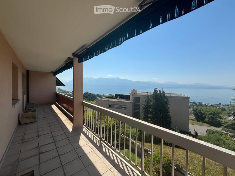 Balcony with tiled floor, white railing, and a scenic view of a lake and mountains in the background.