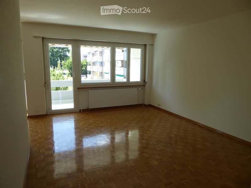Empty room with wooden flooring, large windows, and a radiator. No furniture or equipment present.
