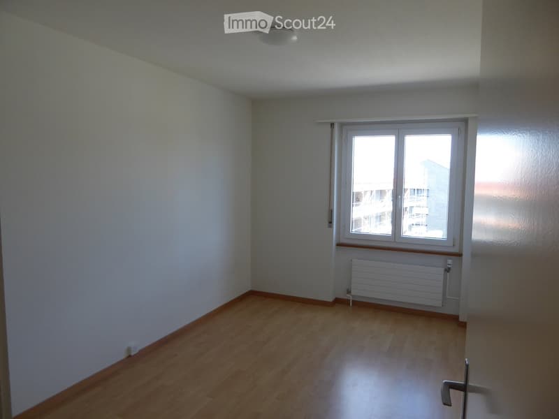 Empty room with wooden flooring, white walls, a large window, and a radiator below it.