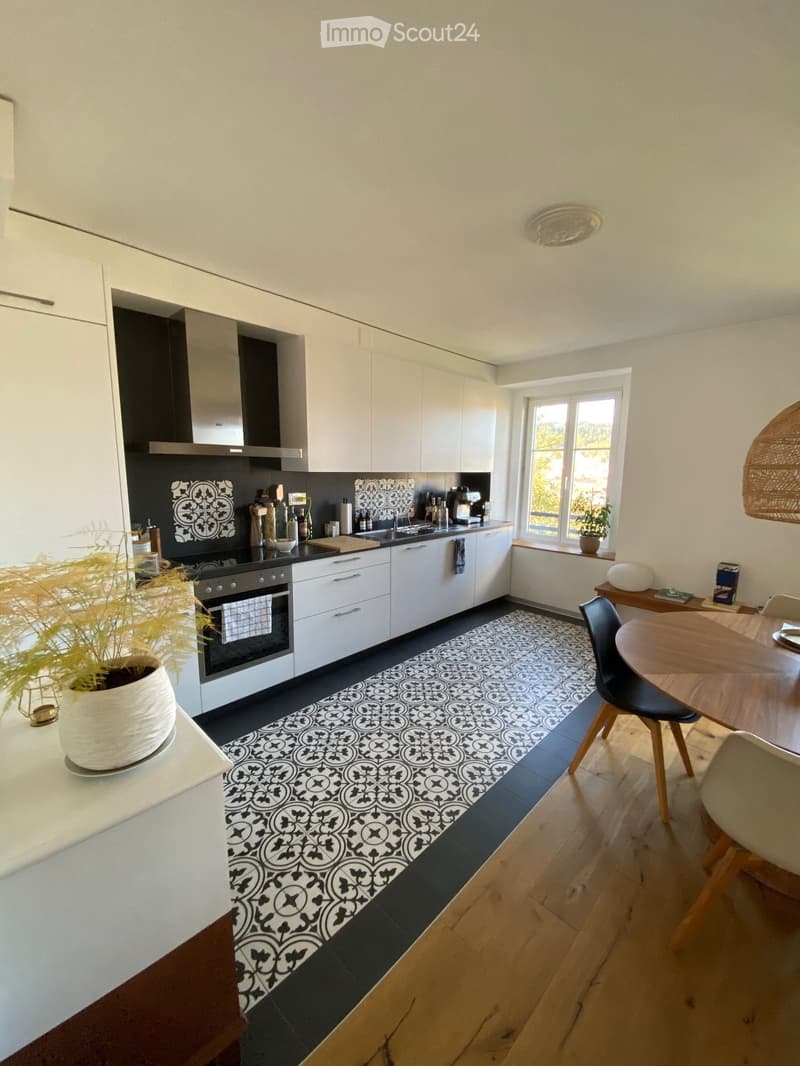 open plan kitchen and dining area, white cabinets, black countertop, black and white tile flooring, dining table and chairs, window