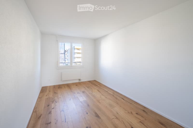 Empty room with light wooden flooring, white walls, and a window with blinds. A radiator is mounted on the wall below the window.