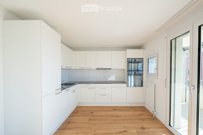 Modern, minimalist kitchen with white cabinets, a black countertop, and a wooden floor. Features a built-in oven and a sink.