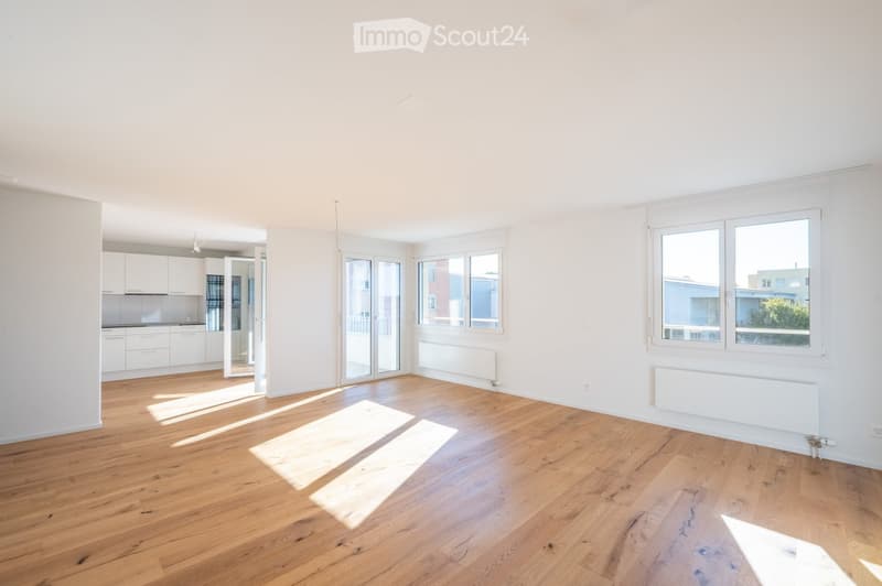 Bright, empty room with wooden flooring, white walls, large windows, and a sliding glass door leading to a balcony.