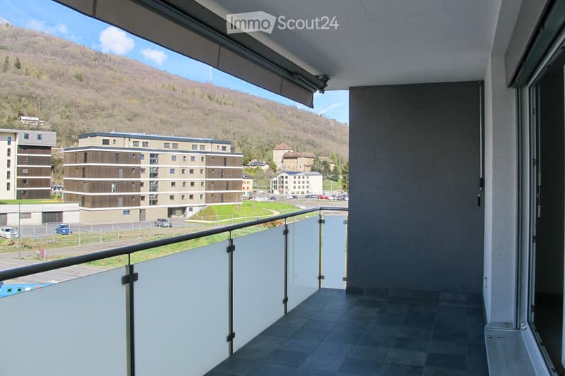 Balcony with tiled floor, glass railing, and scenic view of a town and surrounding hills.