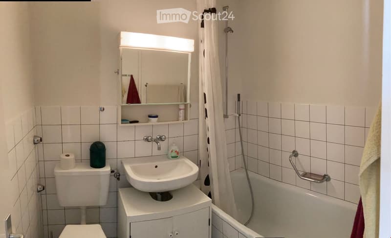 Tiled bathroom with white toilet, white bathtub, white sink, white wall mirror, and black and white shower curtain.