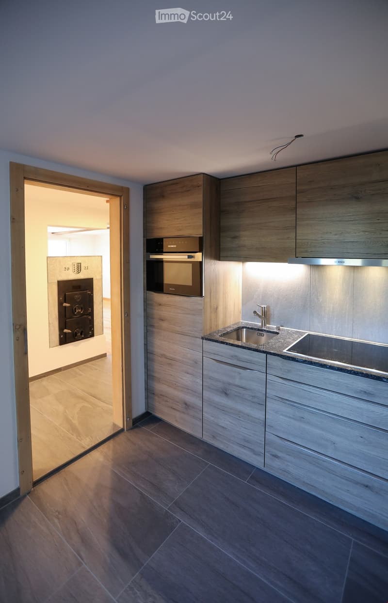 Modern kitchen with wooden cabinets, stainless steel sink, and built-in oven. The space features a clean, minimalist design with a wooden floor and recessed lighting.