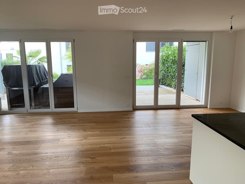 Empty room with wooden flooring, large sliding glass doors leading to an outdoor area, and a covered outdoor grill visible through the doors.