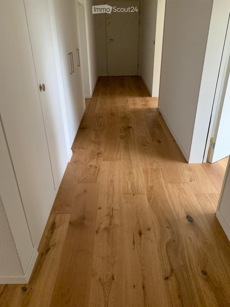 A narrow hallway with light wooden flooring and white walls, featuring closed doors on both sides.