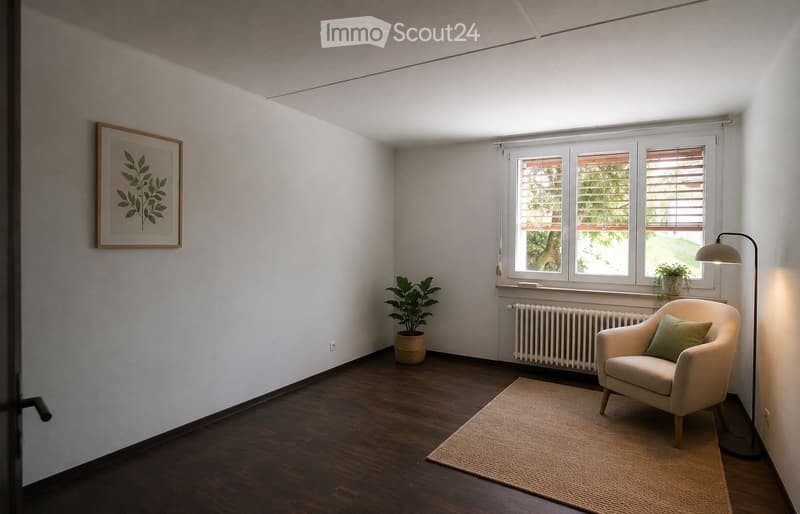 Minimalist living room with wooden flooring, a single armchair, floor lamp, small plant, and a framed picture on the wall.
