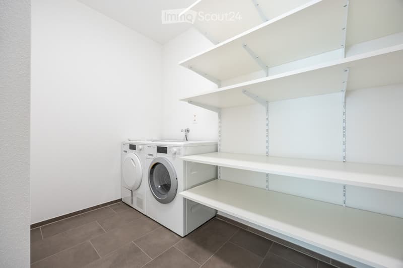 Modern bathroom with white tiled walls, a washing machine and dryer unit, and built-in white shelving units.