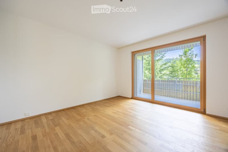 Empty room with wooden flooring and large sliding glass doors leading to a balcony with a view of greenery.