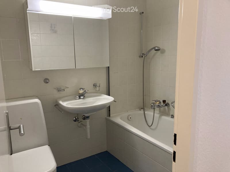Modern bathroom with beige tiled walls, a white toilet, a sink with a mirror cabinet, and a bathtub with a handheld shower.