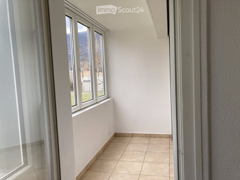 Empty room with tiled floor, white walls, and large windows offering a view of the outside area.