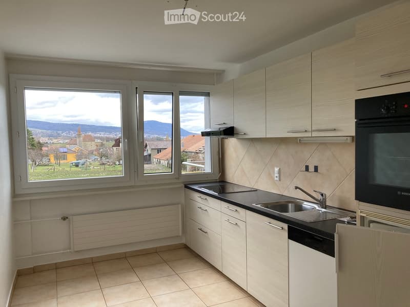 Modern kitchen with light wood cabinets, black countertop, stainless steel sink and faucet, built-in oven and dishwasher, large windows overlooking a scenic view.