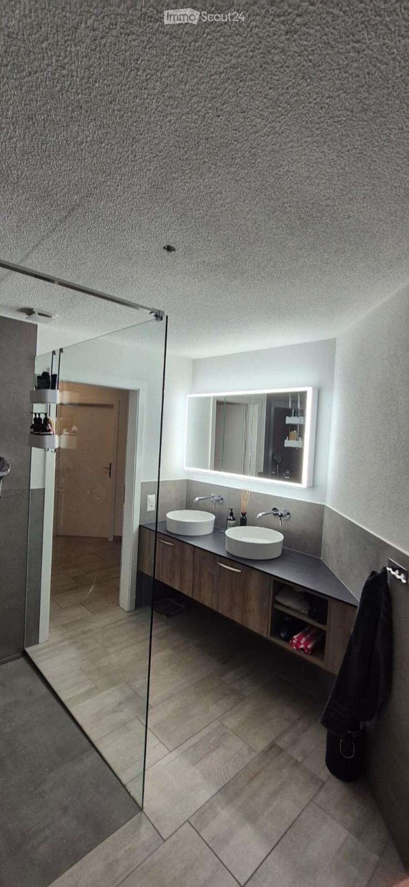 Modern bathroom with a double sink vanity, large mirror, sleek wooden cabinetry, and tiled flooring.