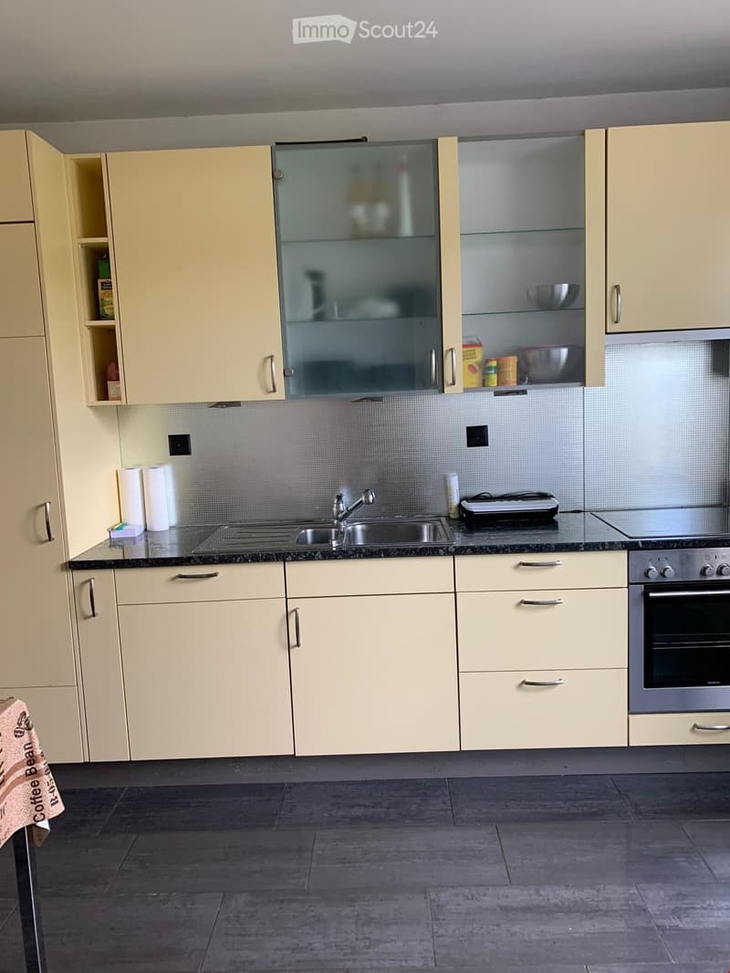 Modern kitchen with light-colored cabinets, stainless steel sink, oven, and countertop items including paper towels and a toaster.