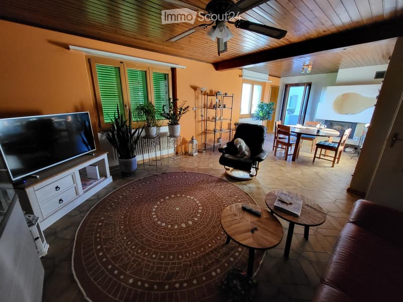 Living room with a large TV, leather sofa, coffee table, dining area with chairs and table, potted plants, and a ceiling fan.