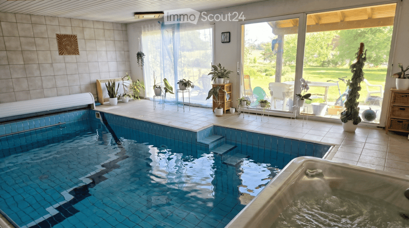 Indoor pool area with a swimming pool, hot tub, chairs, tables, and potted plants, leading to an outdoor patio with more seating and greenery.