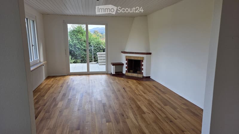 Bright living room with wooden flooring, fireplace, large sliding glass doors leading to a patio, and scenic mountain view.
