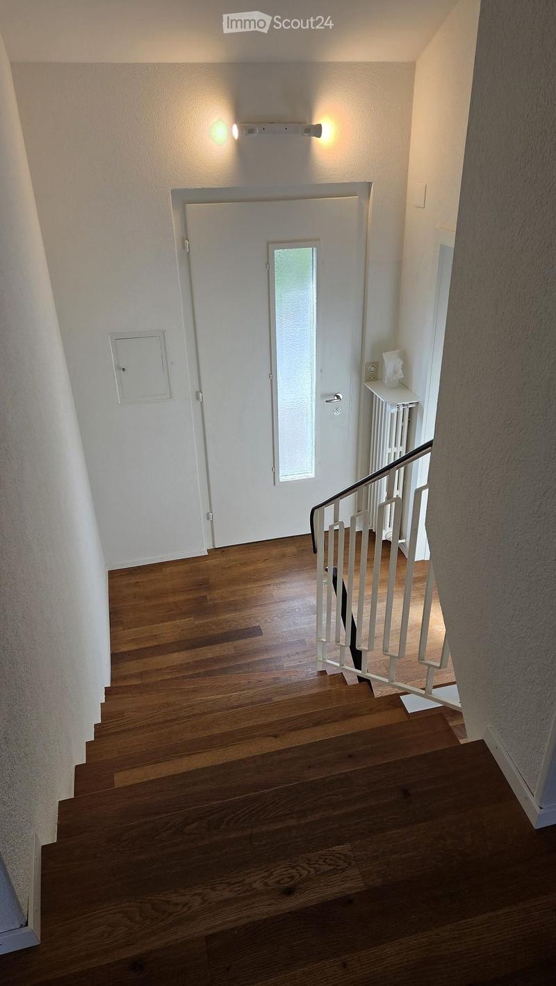 Wooden staircase with white railing, white walls, and a door with a frosted glass panel at the top.