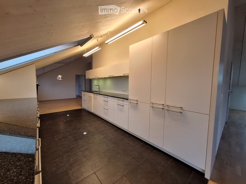 Modern, unfurnished kitchen with white cabinets, dark tiled floor, and built-in appliances. The space features a large skylight and recessed lighting.