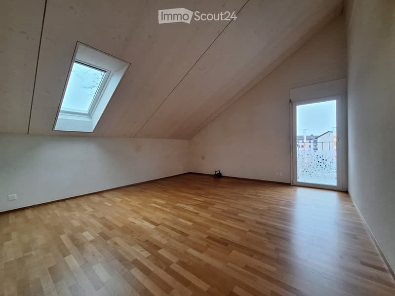 Empty attic room with wooden flooring, white walls, skylight window, and sliding glass door leading outside.