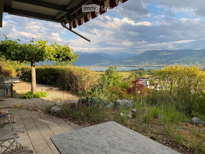 Garden area with a stone table, wooden chair, and scenic mountain view.