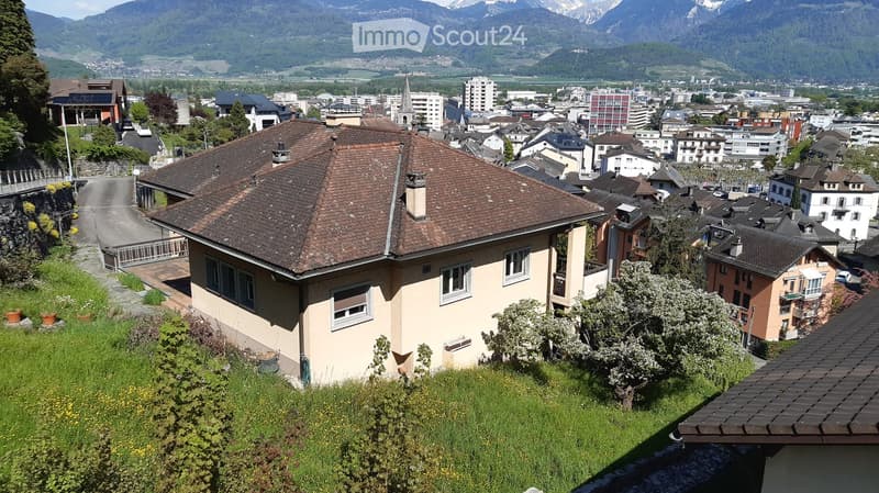 A view of a town with houses, a road, and mountains in the background.