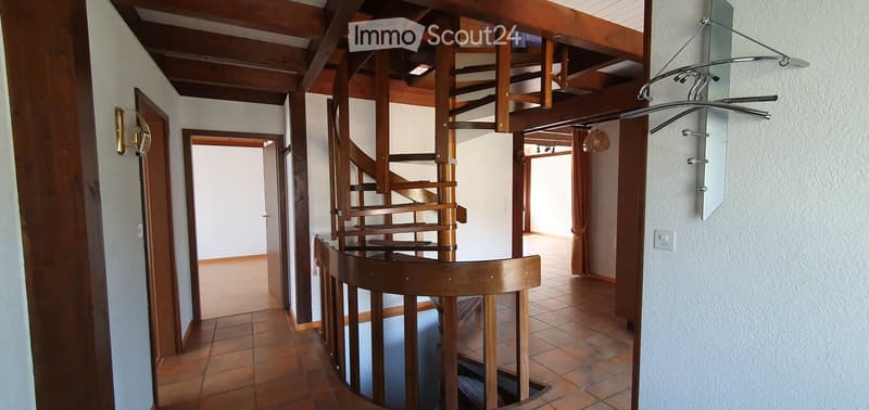 Spacious hallway with a wooden spiral staircase leading to an upper level, tiled flooring, and several doors opening to adjacent rooms.