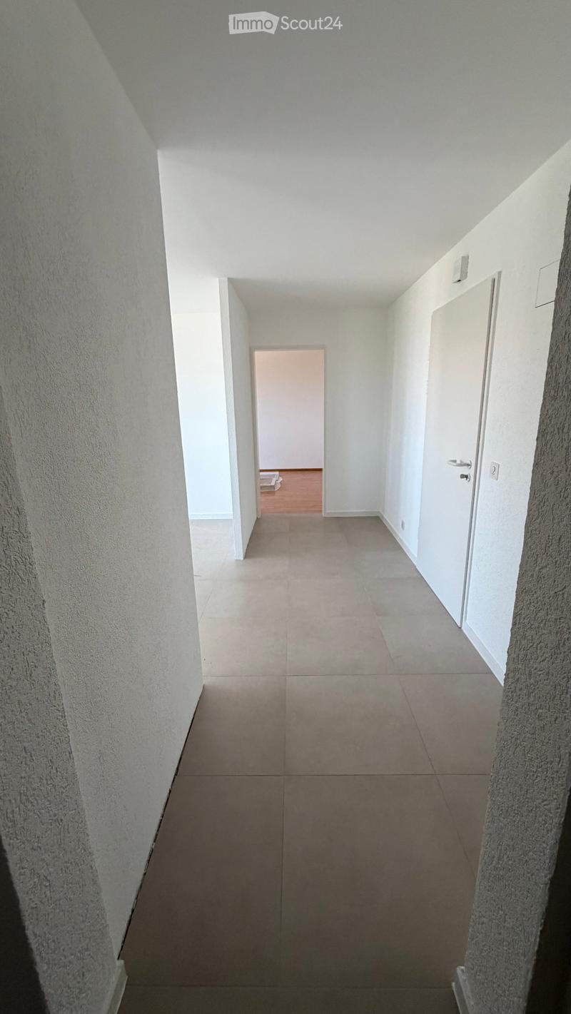 Empty hallway with tiled floor, white walls, and a door at the end leading to another room.