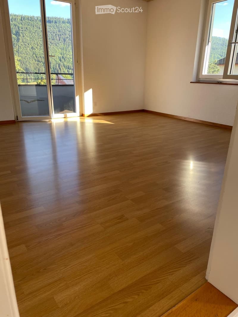 Empty room with wooden flooring, large windows, and a sliding glass door leading to a balcony with a scenic view.