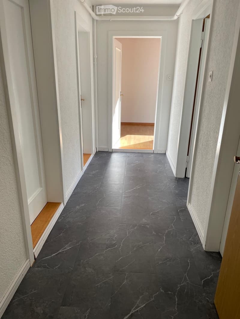 Clean, modern hallway with dark grey marble tiles, white walls, and several doors leading to other rooms.