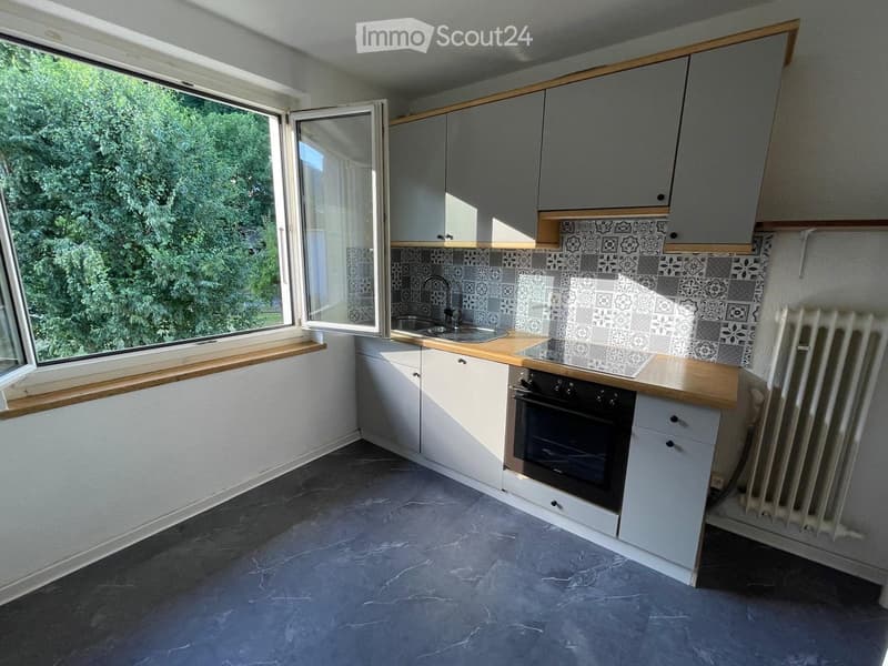 Modern kitchen with white cabinets, wooden countertops, a sink, and an oven. Features a large window with a view of greenery outside.