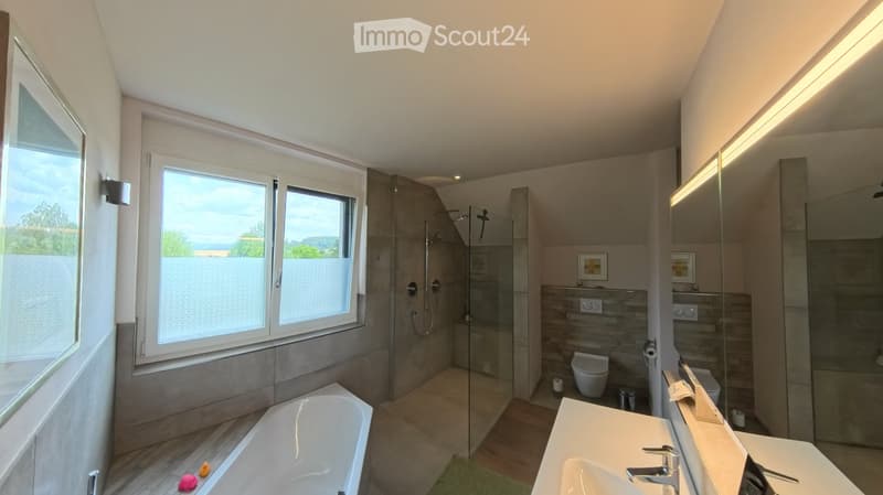 Modern bathroom with a bathtub, sink, toilet, and glass-enclosed shower. Features large windows with a scenic view, sleek fixtures, and a neutral color palette.
