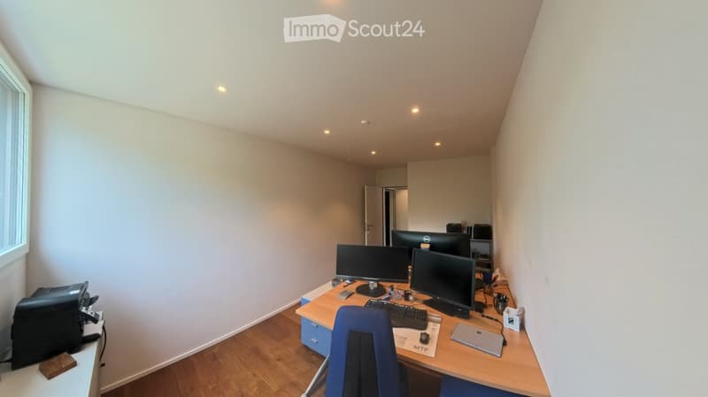 Office space with wooden flooring, white walls, and multiple monitors on a desk. Includes a blue chair, laptop, keyboard, mouse, and printer.
