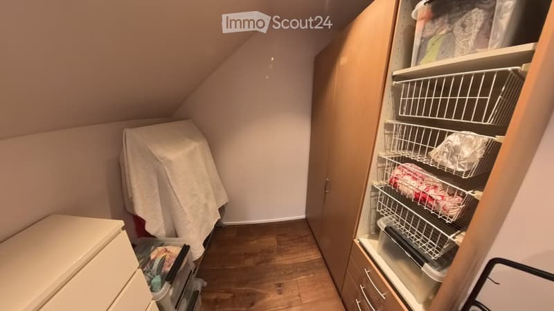 An attic storage space with wooden flooring, slanted ceilings, and built-in shelving units containing plastic bins and baskets.