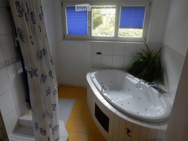 Bathroom with a large bathtub, multiple faucets, a shower curtain with blue designs, and a potted plant on the edge of the tub.