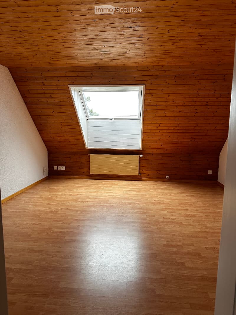 empty room with wooden flooring, wooden paneling on the walls, a window and a radiator