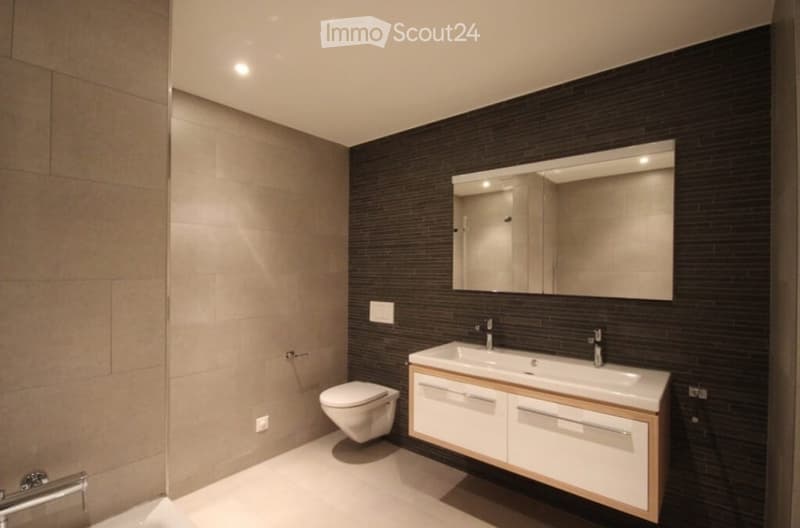 Modern bathroom with dark brick walls, white sink, mirror, and toilet.